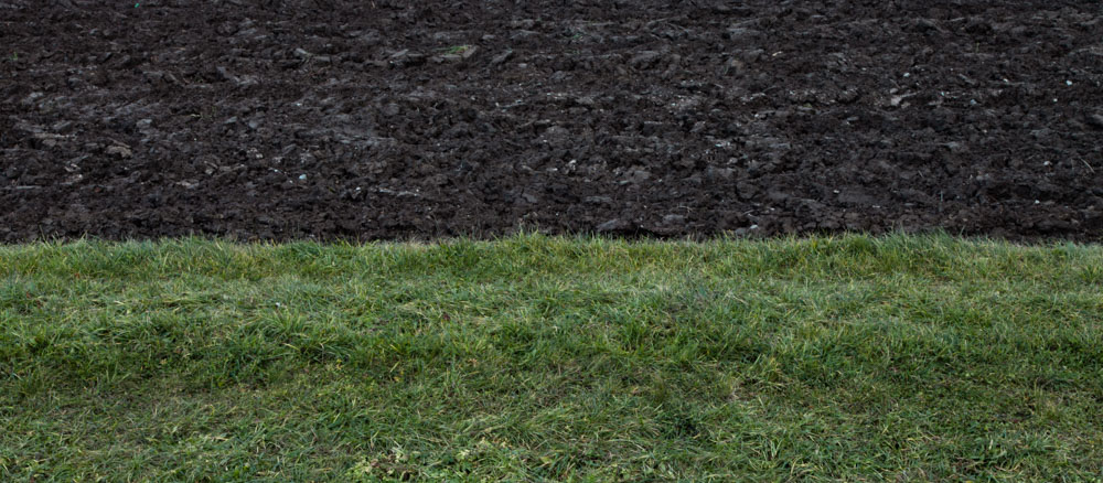 minimalistic horizontal image, seeming two-dimensional, showing freshly ploughed earth and grass
